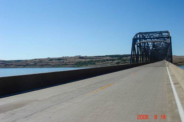 Rolling grassland along the highway with distant hills and farm buildings