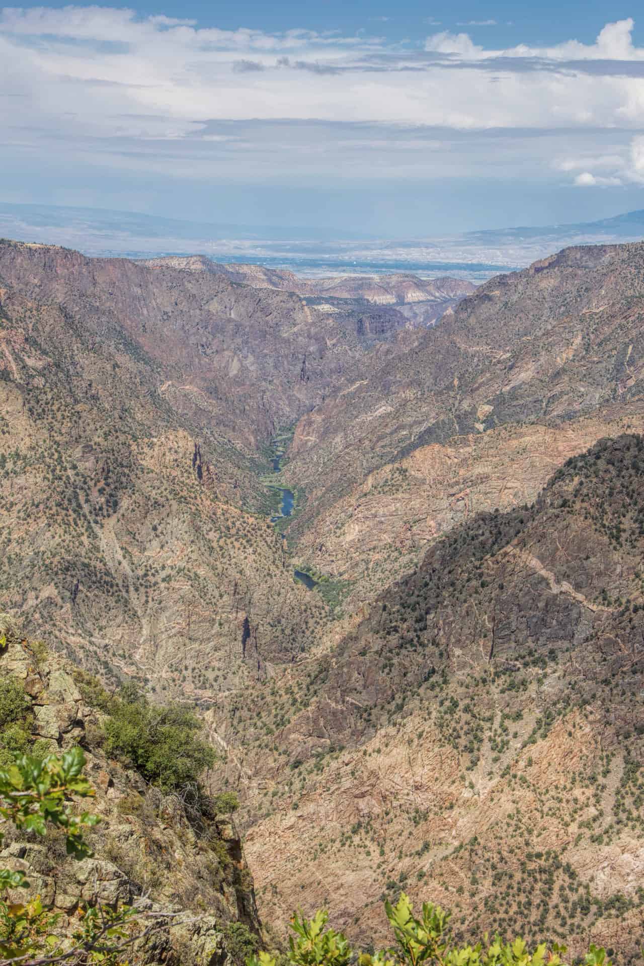 A deep, narrow canyon view with the Gunnison River visible far below amid steep, rugged walls