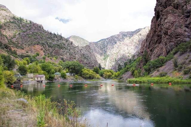 The Gunnison River lined with buoys, flanked by canyon walls and a small building near the water's edge