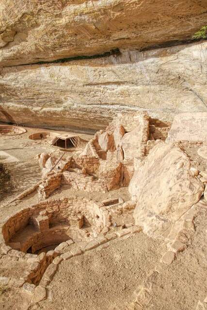 Ancestral Puebloan cliff dwelling ruins built into a sandstone alcove, with round kivas and stacked stone walls