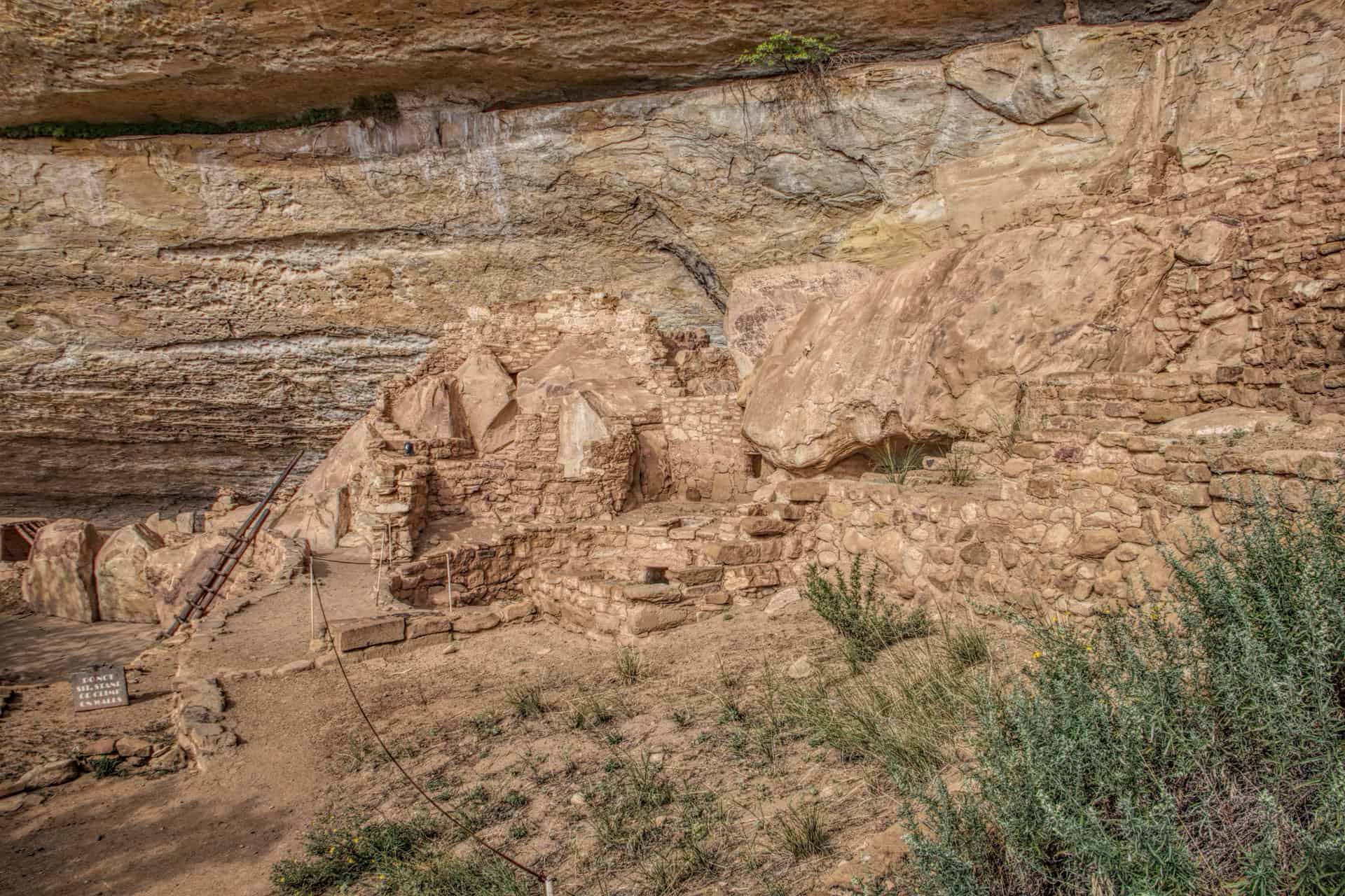 Stone masonry ruins of a cliff dwelling tucked beneath an overhanging sandstone cliff