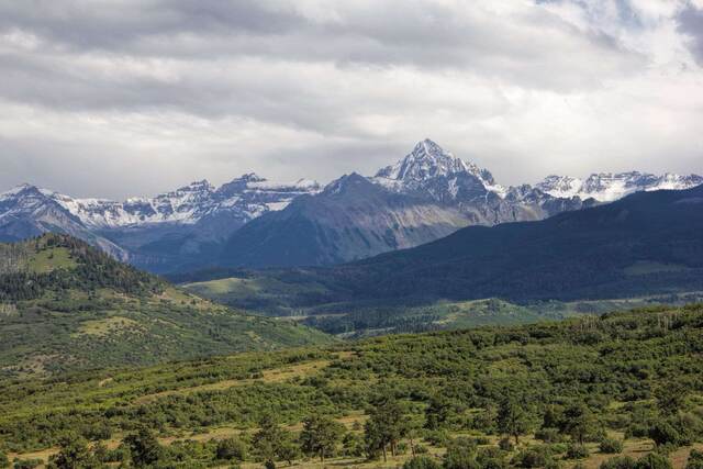 Snow-dusted peaks of the Sneffels Range towering above green foothills and forest