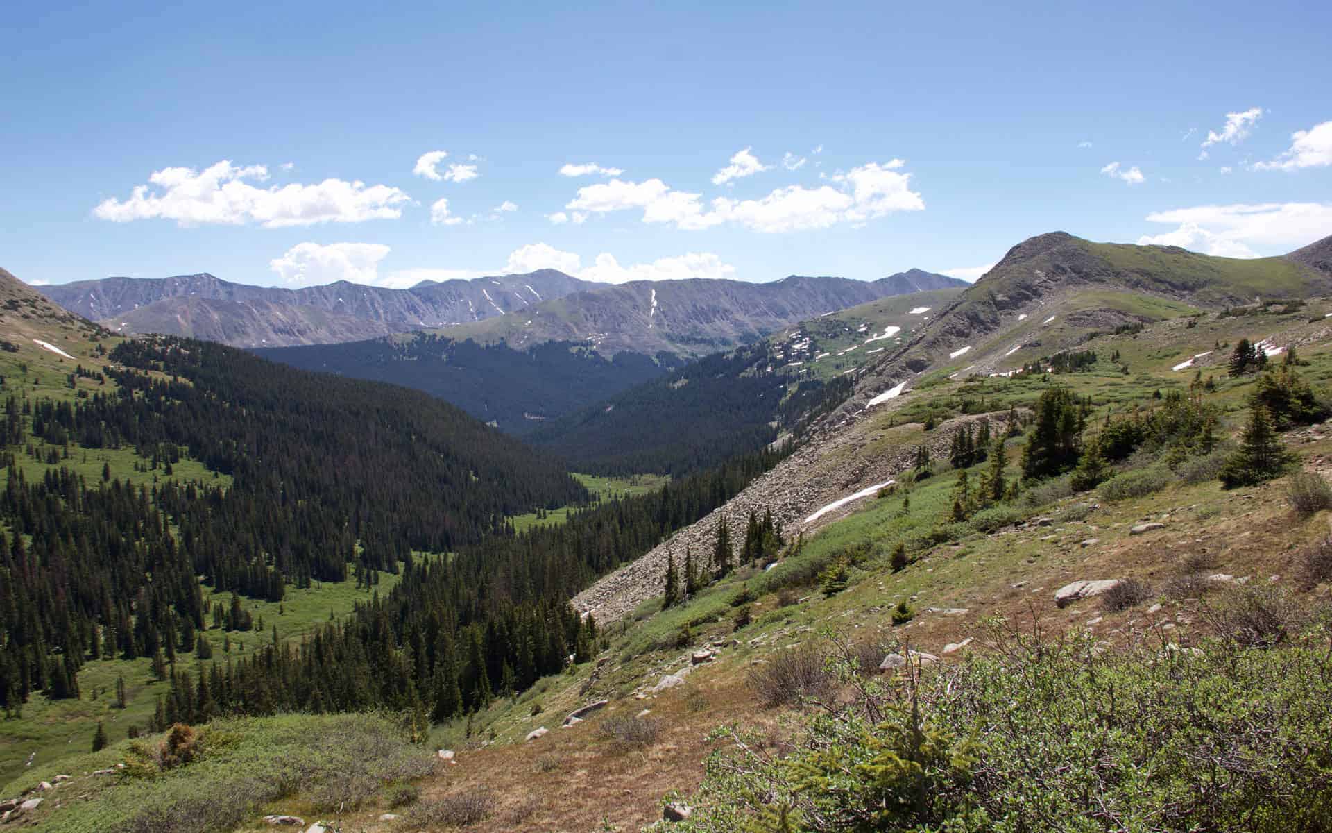A sweeping view down a forested valley toward layered mountain ridges under a partly cloudy sky
