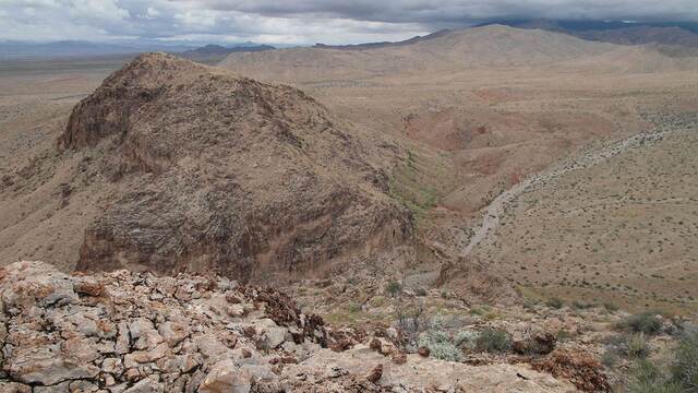 A mountain peak in the foreground overlooking a valley wash under gathering storm clouds