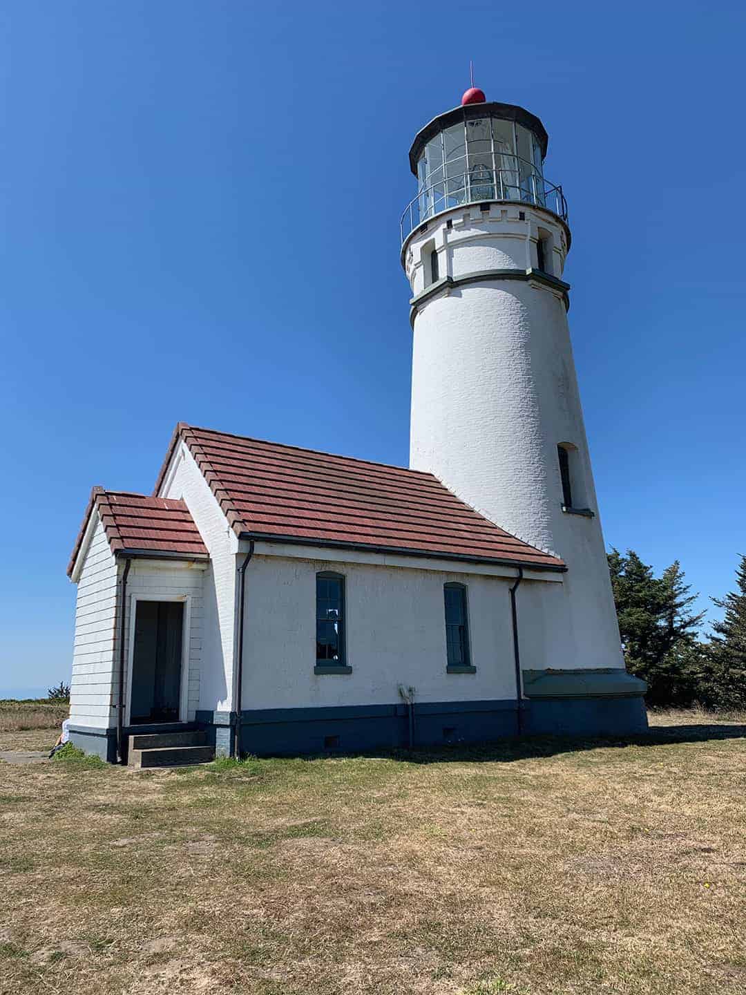 Cape Blanco Lighthouse and the attached keeper's quarters building, viewed from the grassy bluff