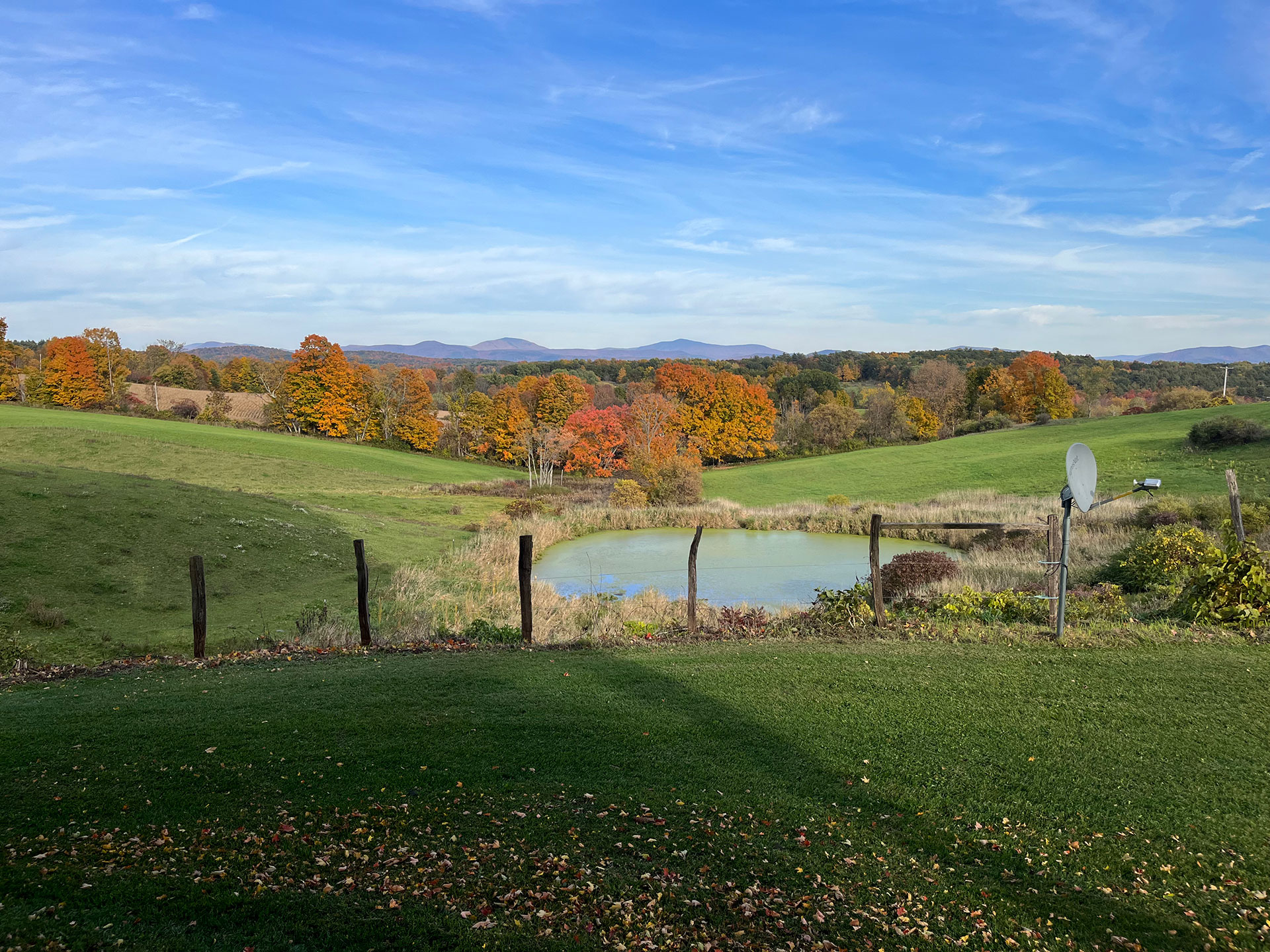 Rolling farmland with a small pond and fall-colored trees in the distance