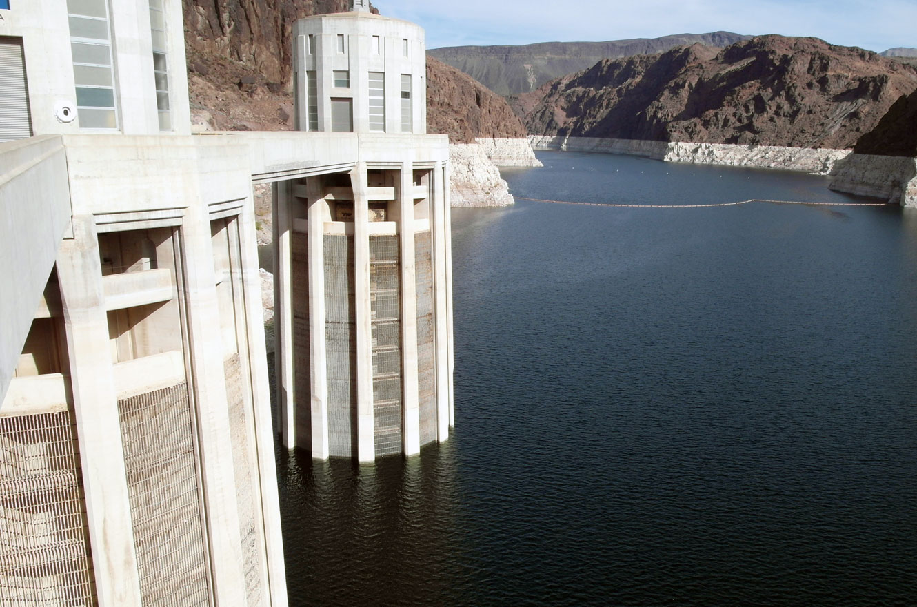 A close-up of two of Hoover Dam's intake towers rising from Lake Mead, with a mineral-stained bathtub ring marking the canyon walls above the water