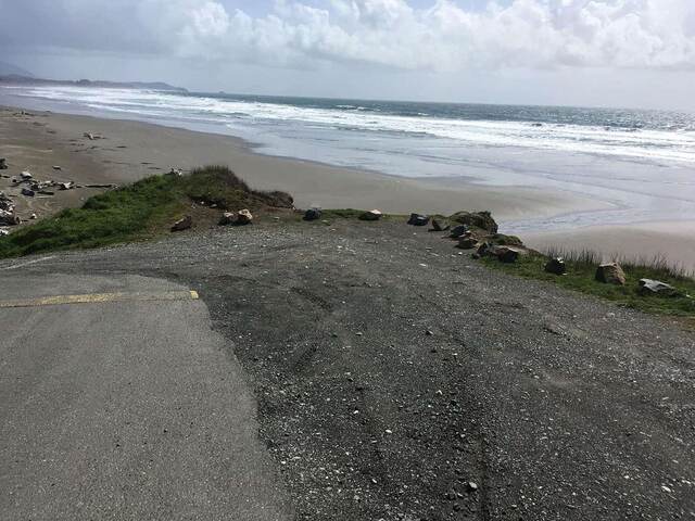 A paved beach access path leading down to the ocean, framed by dune grass and dark volcanic rocks