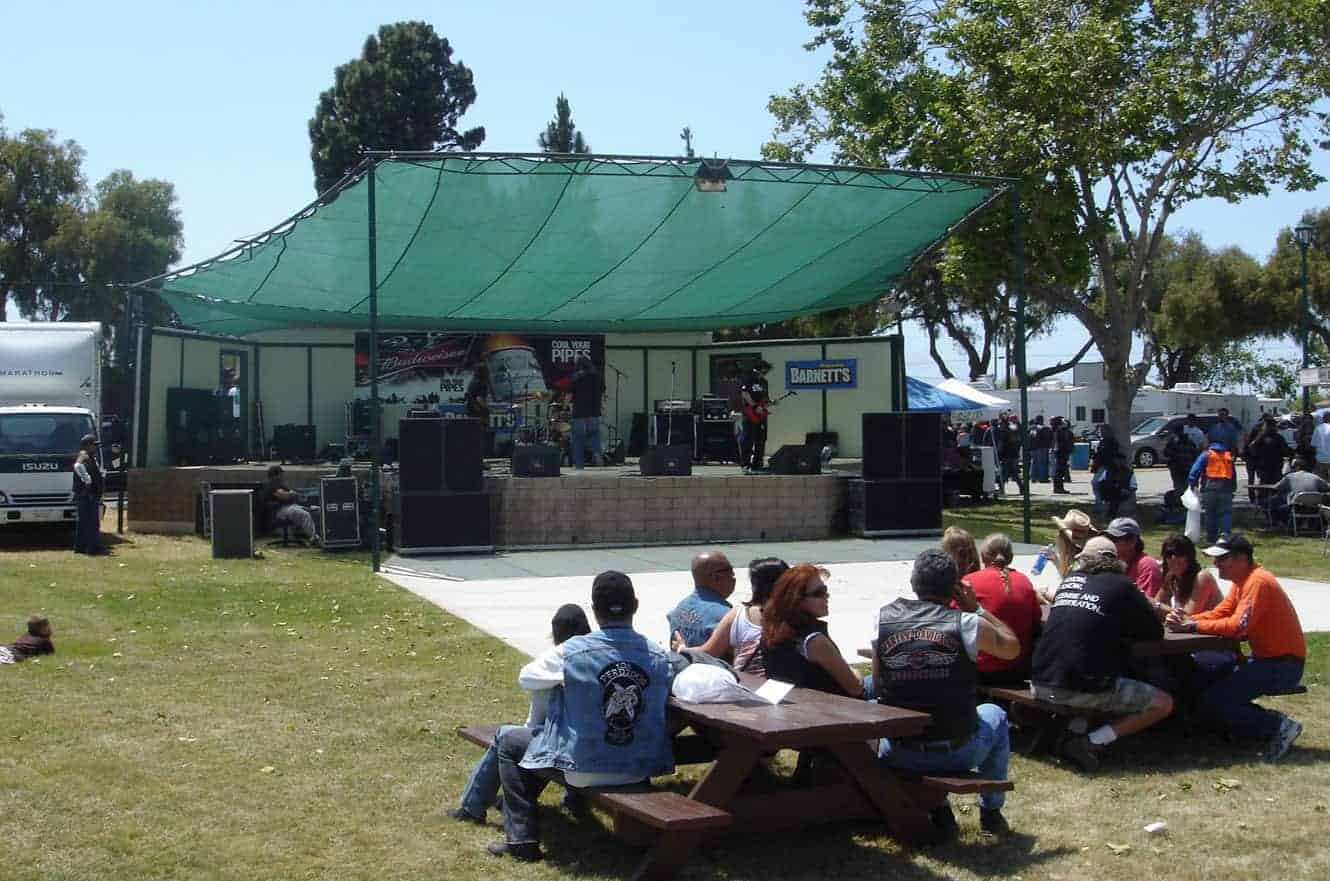 A band performing on an outdoor stage at a motorcycle rally in Santa Maria, California, with bikers gathered at picnic tables
