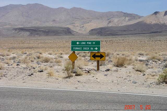 A road sign pointing toward Lone Pine and Furnace Creek in the barren desert near Death Valley