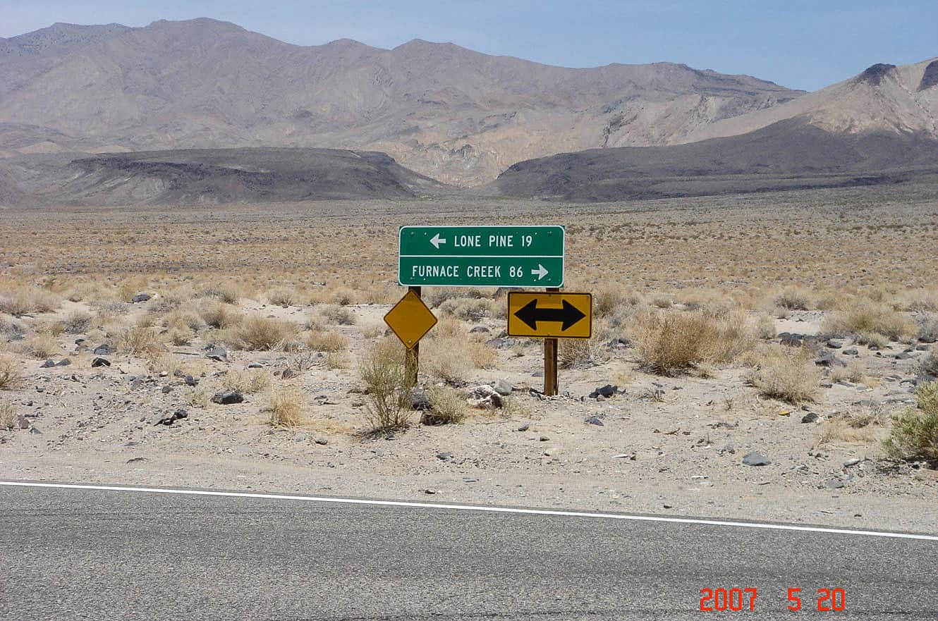A road sign pointing toward Lone Pine and Furnace Creek in the barren desert near Death Valley