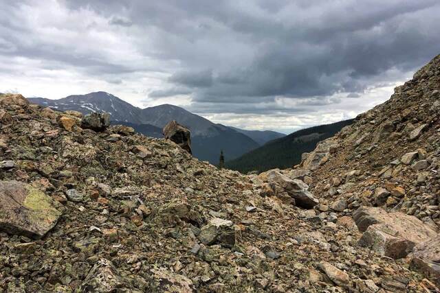 A rocky outcrop on a ridge overlooking a forested valley, with dark storm clouds and distant peaks beyond