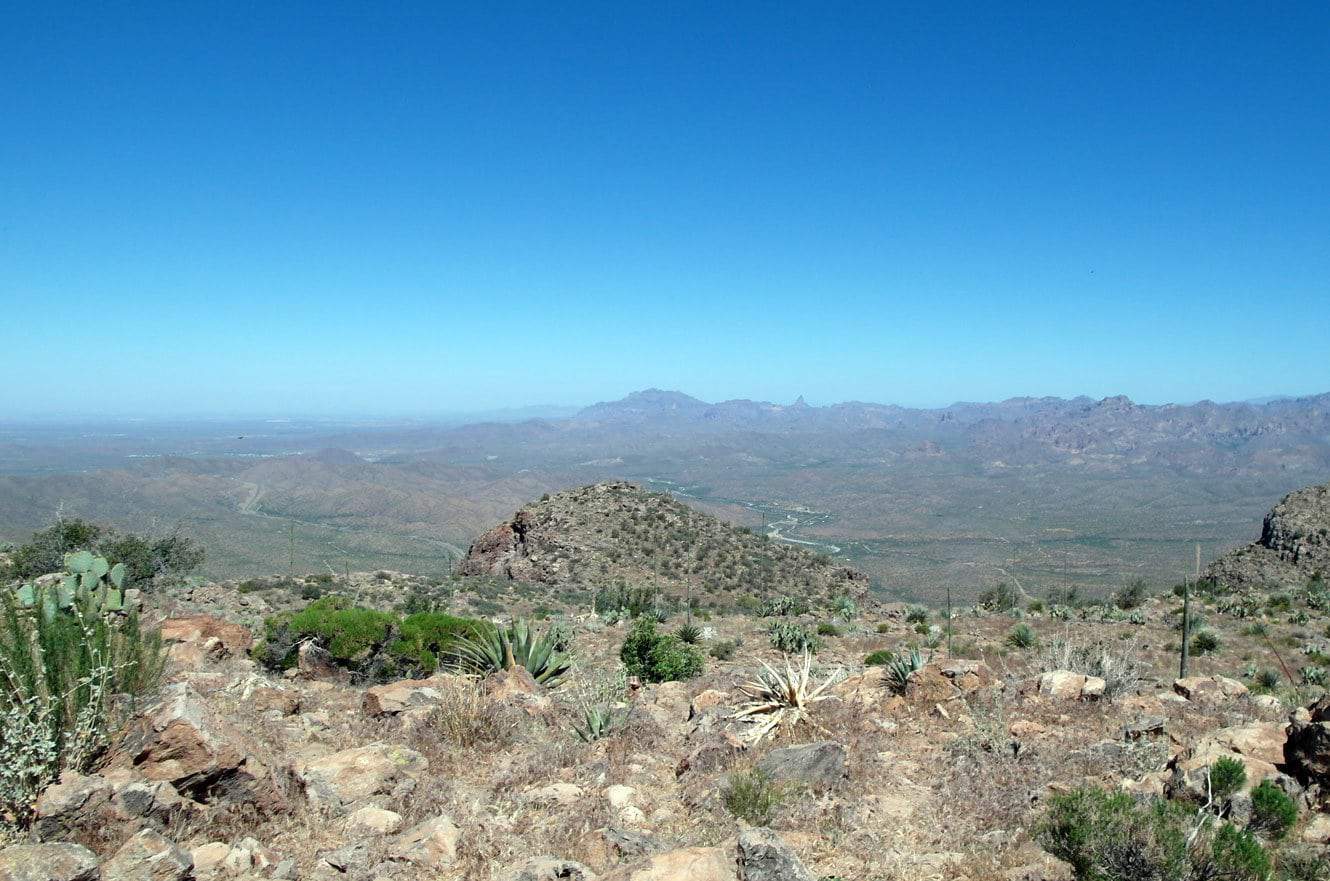 A hazy view over the desert valley and surrounding mountains partway up Picketpost Mountain, with agave in the foreground