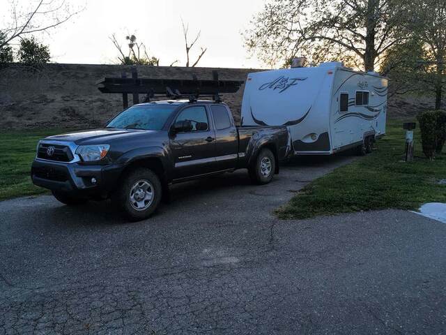 A truck towing a travel trailer parked in the grassy campground at Dos Reis State Park at dusk