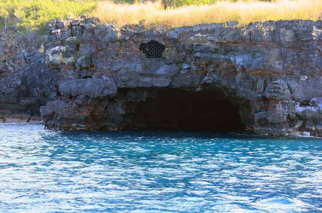 A sea cave opening in the lava cliffs, with a small grated opening in the rock above