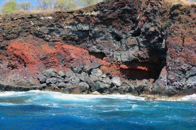 Red and black layered lava rock exposed along the cliff face