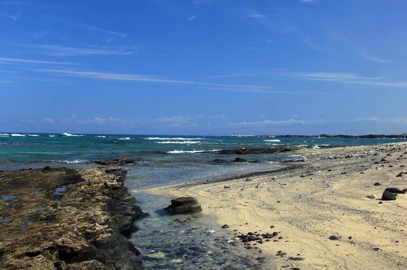 A rocky tide pool and pale sand beach along the coast at Kekaha Kai State Park