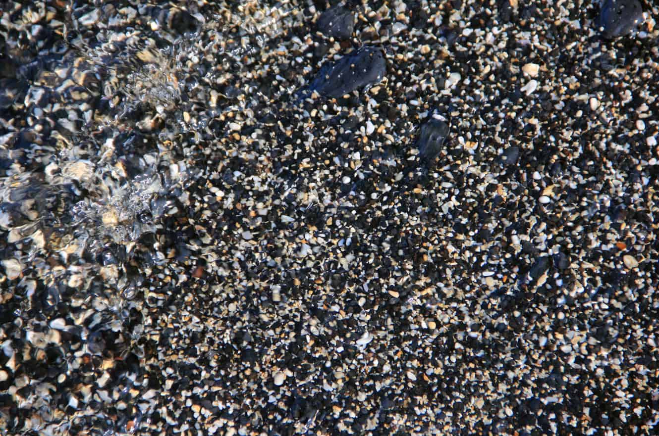 Close-up of small black and tan pebbles at the water's edge
