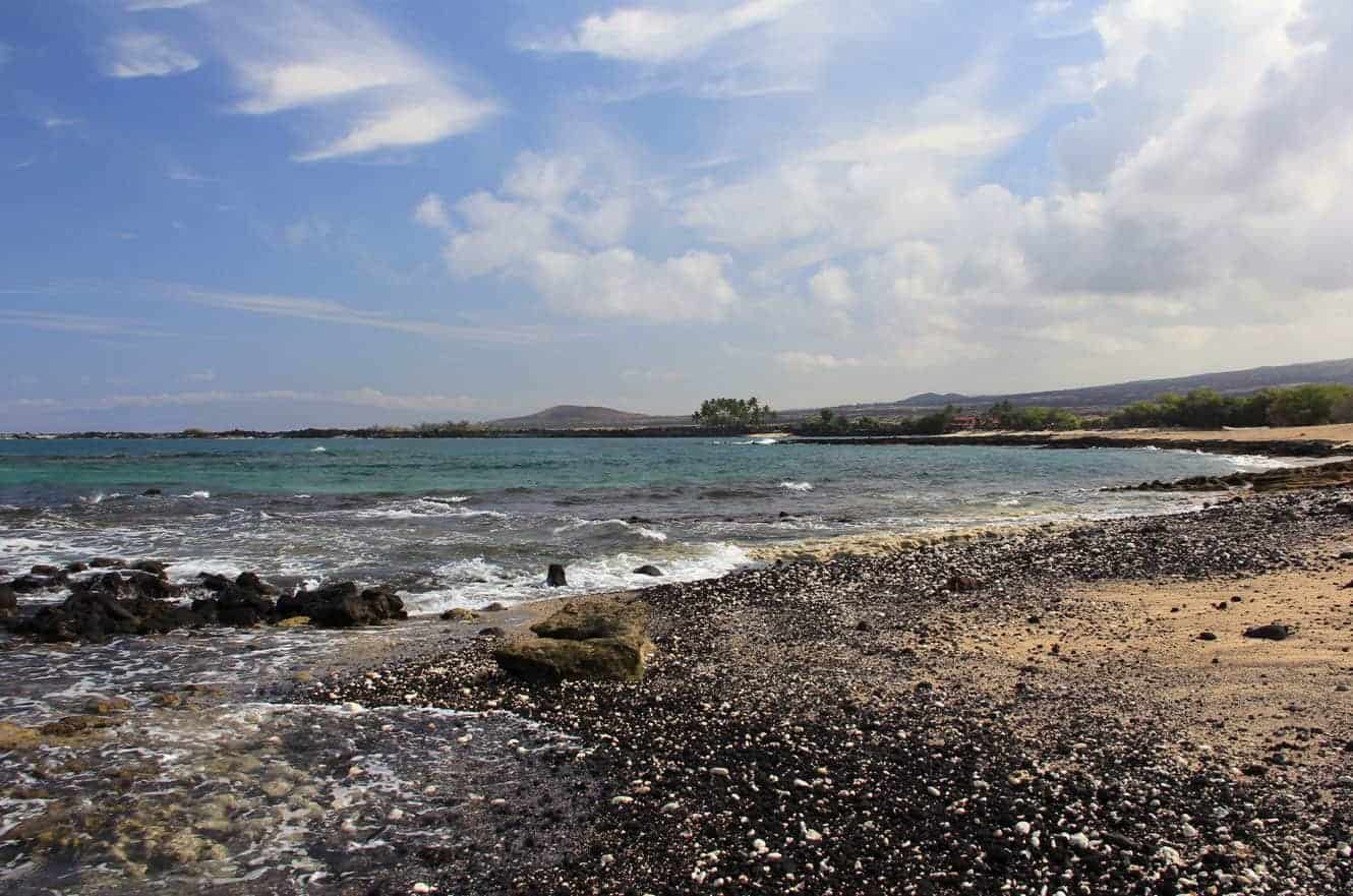 A wide beach cove with distant palm trees and mountains along the coastline