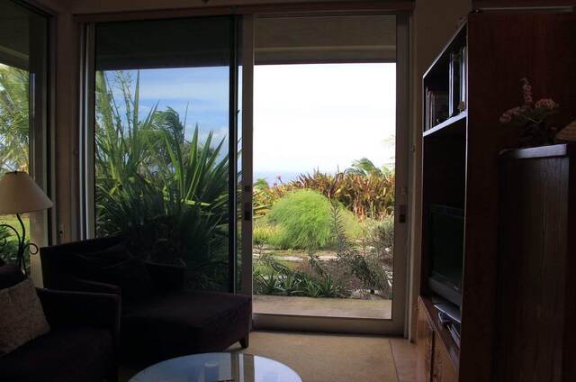Interior view through sliding glass doors overlooking a lush garden with palm trees and ocean beyond