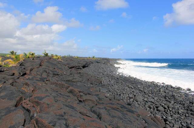 A rugged black lava rock shoreline with waves breaking along the coast