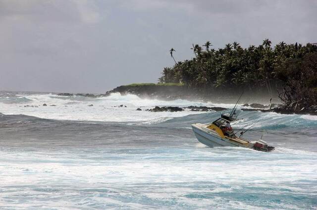 A fishing boat heading out past a rocky, palm-lined point at Isaac Hale Park with big surf breaking